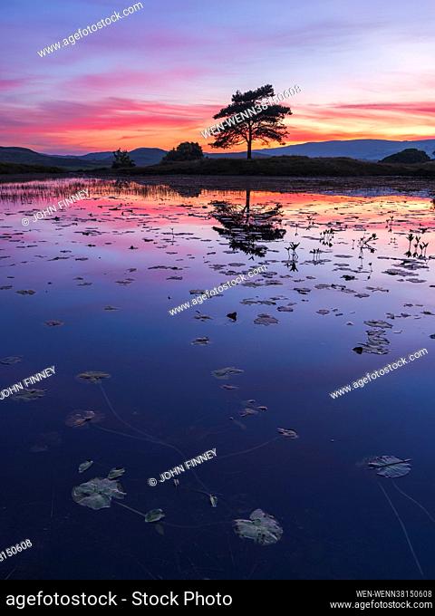 Vivid colours across the sky at dusk reflect on the water at Kelly Hall Tarn near the village of Torver and Coniston Water in Cumbria