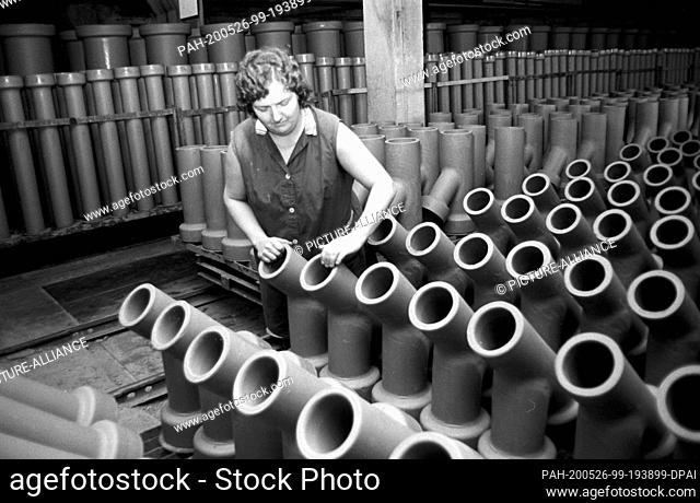 22 August 1986, Saxony, Torgau: Ceramic tubes are standing in the delivery hall of the stoneware factory in Torgau in the mid-1980s, inspected by an employee