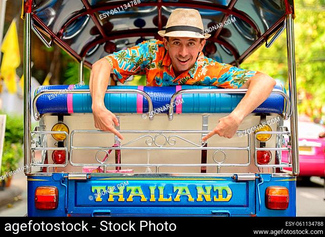 Portrait of young handsome tourist man riding tuk tuk as local public transportation in Bangkok city