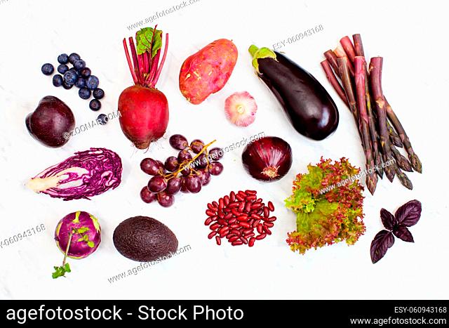 Raw purple vegetables and fruits over white marble background. Top view, flat lay