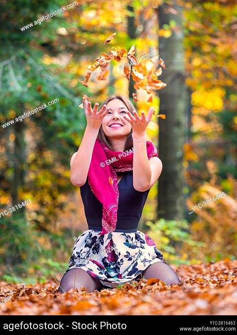 Young woman in nature playful with Autumnal fallen leaves