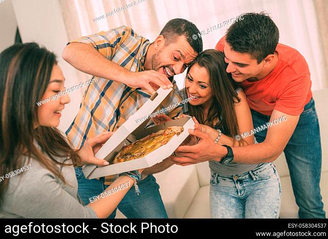 Four cheerful friends enjoying pizza together at home party. Selective focus
