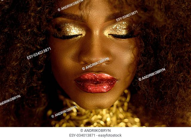 Surreal close-up portrait of young african american female model with gold glossy makeup. Face art. Fashion concept