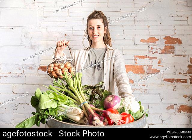 Smiling owner with eggs and vegetables in front of brick wall