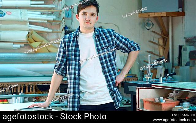 Portrait of a young male worker, standing and looking at camera seriously in workshop. Professional shot in 4K resolution. 083. You can use it e. g