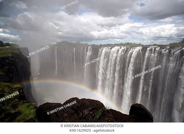 Victoria Falls with rainy clouds, view into the canyon of the Zambezi river, people seen on the left edge of the rocks, Zimbabwe