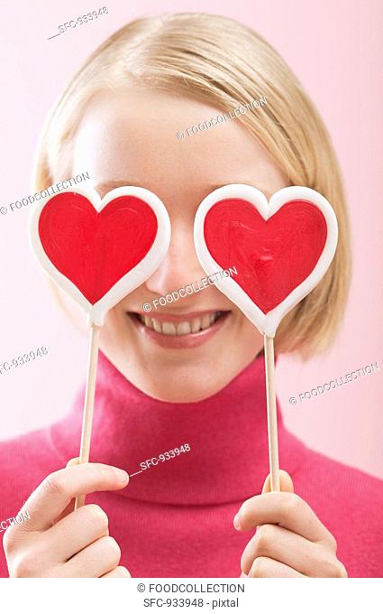 Love is blind: woman with heart-shaped lollipops in front of her eyes
