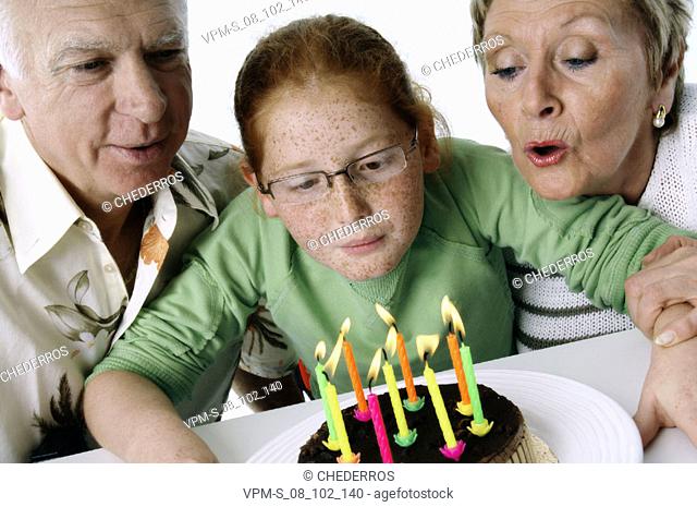 Close-up of a granddaughter blowing out candles on a birthday cake with her grandparents
