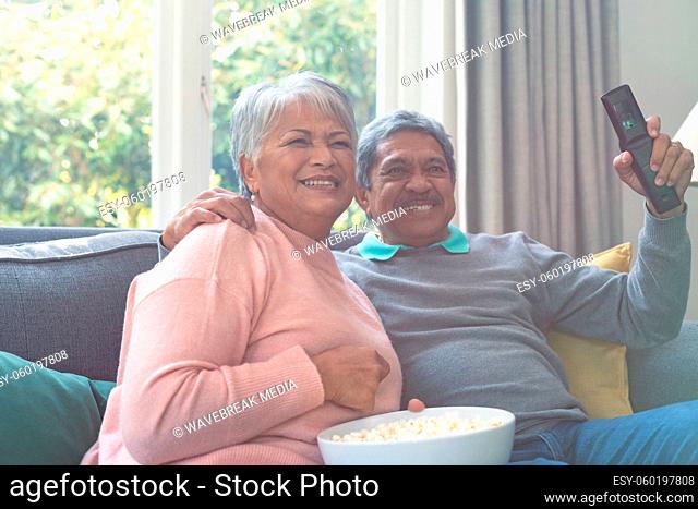 Two diverse senior couple sitting on sofa, watching tv and having fun