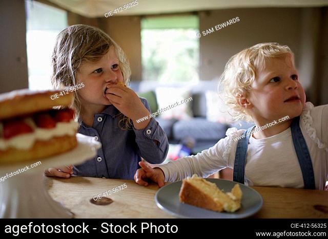 Cute sisters eating strawberry cake at dining table