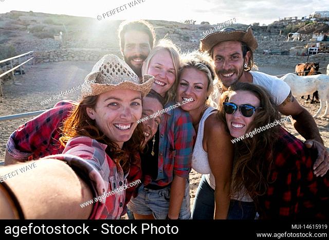 group of seven people together having fun in a ranch with horses - caucasian people taking a selfie smiling and laughing togetherness - enjoying