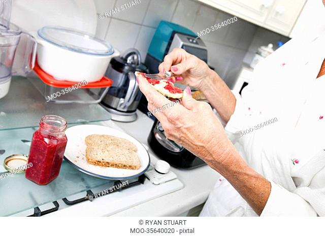 Cropped image of senior woman applying jam on toast in kitchen