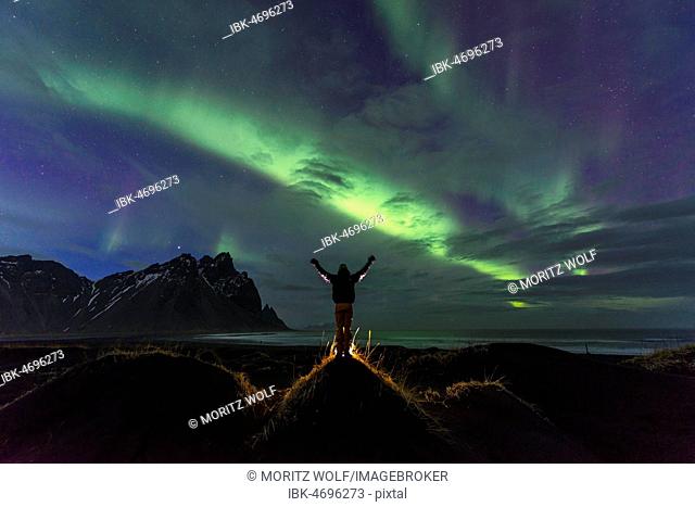 Night shot, man watching Northern Lights (Aurora borealis), Black sand beach, mountains Klifatindur, Eystrahorn and Kambhorn, headland Stokksnes