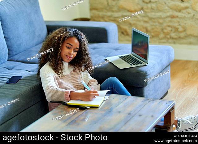 Young woman writing in notepad at table in living room at home
