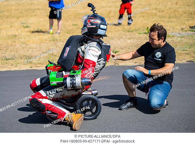 05 August 2018, Germany, Bottrop: Aliatdin Sen (R), longtime friend and helper, supports Dirk Auer on his bobby car before the test drive