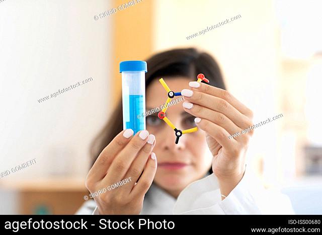 Chemist holding test tube and molecular model, focus on foreground