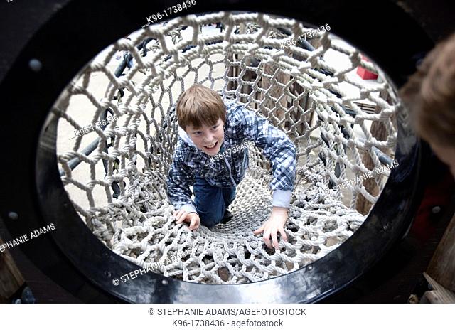 boy laughing while climbing a rope tunnel
