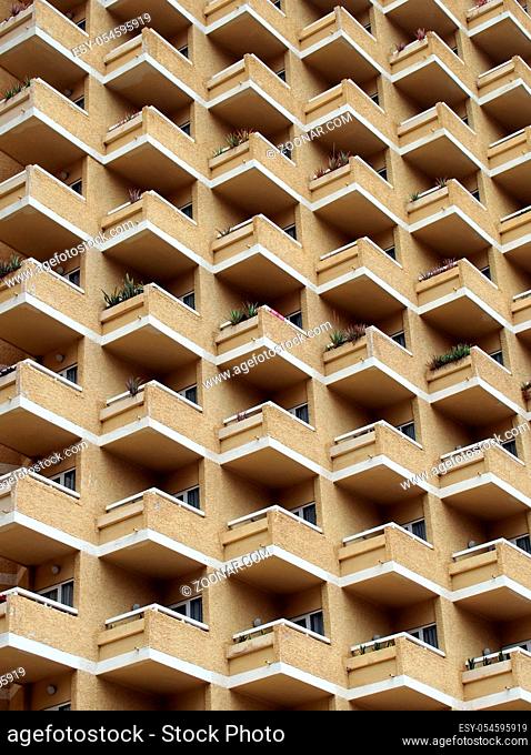 large highrise modern apartment building with large number of repeating geometric balconies in stone yellow colors