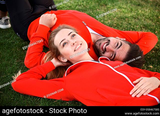 Portrait of sport man and woman in red jackets resting and relaxing in green park. Happy couple lying face to face on green grass