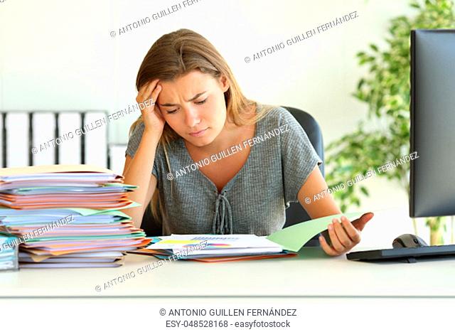 Front view portrait of a worried employee reading bad report sitting in her desktop at office