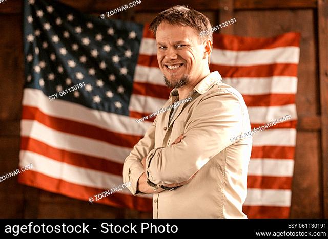 Successful American Entrepreneur Attractive Light-Skinned Man With Beard Laughs Cheerfully In The Office On American Flag Back, Patriotism Concept
