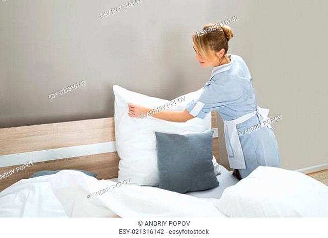 Female Housekeeping Worker Putting White Pillows In Bedroom