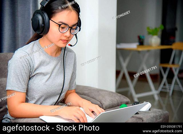 Asian young woman student with headphones sitting on the sofa look at laptop happy study online class college learning internet education