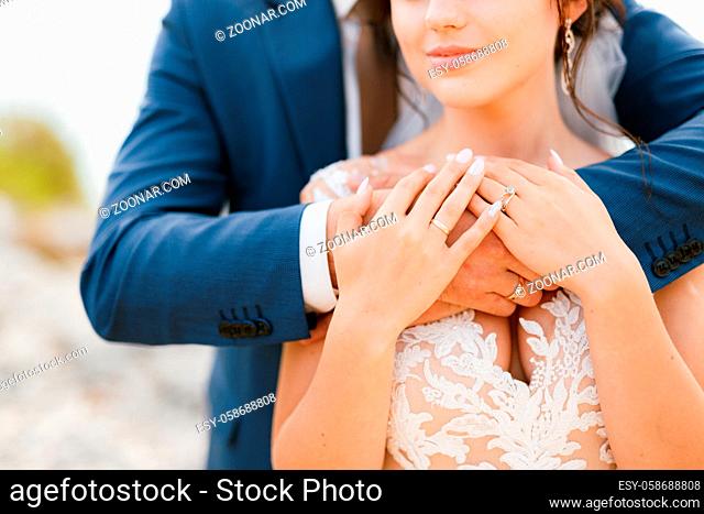 The groom gently hugs the bride by the shoulders, the bride put her hands on the groom's arms, close-up. High quality photo