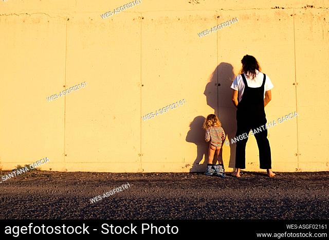Father and son urinating on yellow wall