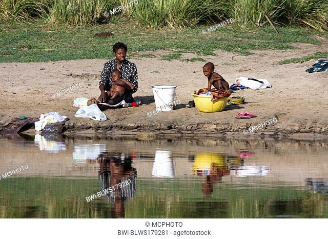 African woman washing her children at shore of the river, Namibia, Kawango River