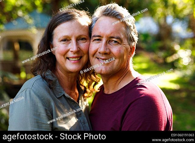 Portrait of happy senior caucasian couple embracing, looking to camera in sunny garden