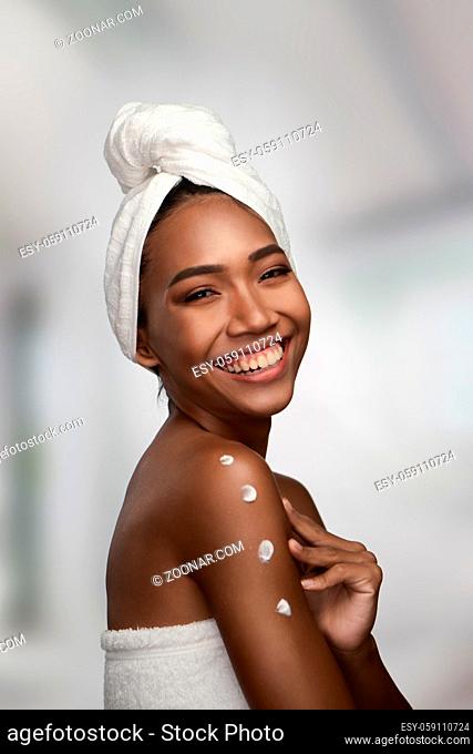 Close-up portrait of a beautiful smiling woman with clean skin applying cream on her shoulder isolated on white background