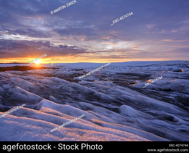 Midnight sun on the ice sheet. The brown sediment on the ice is created by the rapid melting of the ice. Landscape of the Greenland ice sheet near Kangerlussuaq