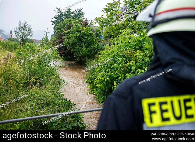 29 June 2021, Baden-Wuerttemberg, Staufen im Breisgau: A firefighter checks the water level at a flooded creek. Heavy rainfall in the early afternoon of 29