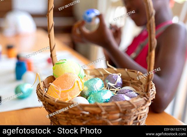 Basket of colourful eggs with african american girl painting in the background