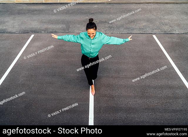 Smiling businesswoman with arms outstretched balancing on road marking