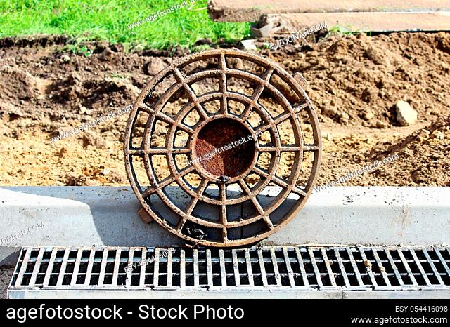 rusty round hatch and grate for rainwater on the side of the city road. repair and expansion of the road. reportage photography