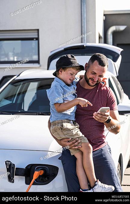 Father and son checking smartphone by charging electric car