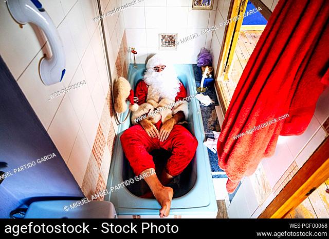 Man wearing Santa Claus costume lying in bathtub at home