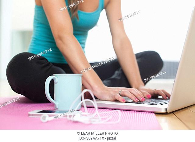 Young woman on yoga mat using laptop