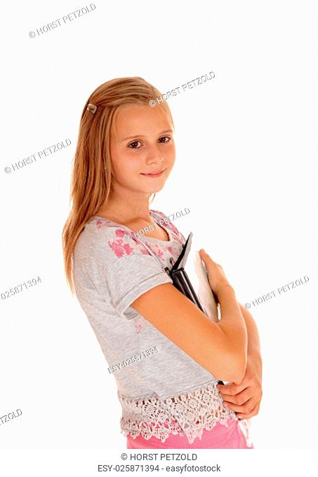 A young smiling blond girl a pink pants, holding her folders.close to her chest, isolated for white background.