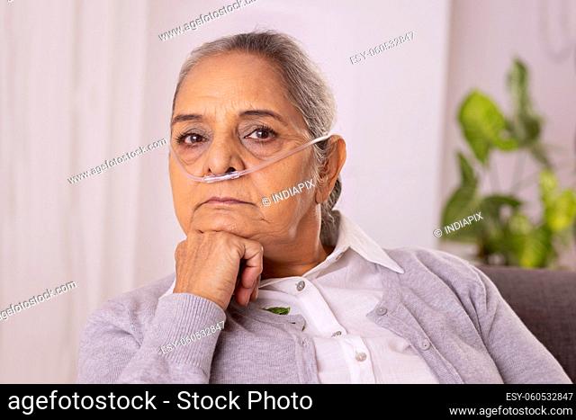 Old woman sitting on sofa with nasal cannula at home
