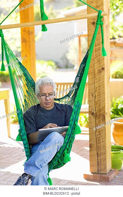 Caucasian man using digital tablet in green hammock