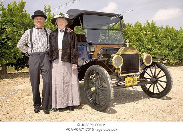 Couple dressed in old-fashioned clothing standing in front of their antique car in Santa Paula, CA