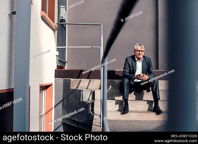 Senior businessman holding drinking glass on staircase