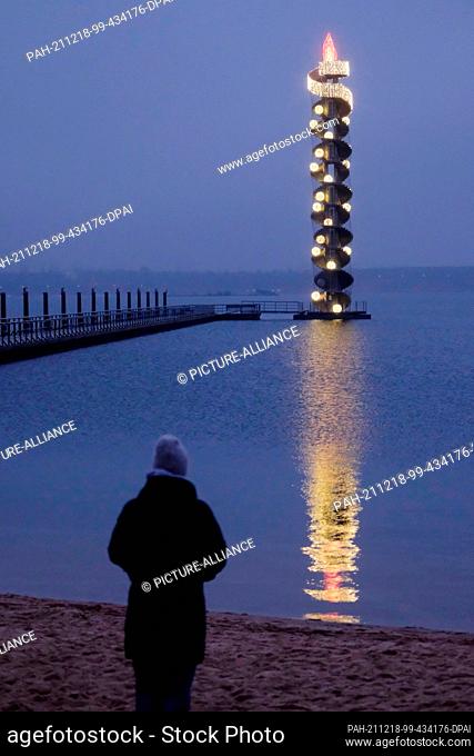 18 December 2021, Saxony-Anhalt, Muldestausee: A walker stands by the Goitzsche Lake with the water level tower in the background