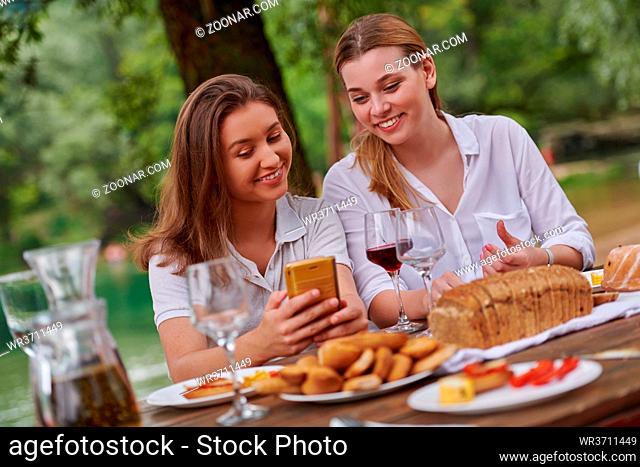two young happy girlfriends having picnic french dinner party outdoor during summer holiday vacation near the river at beautiful nature