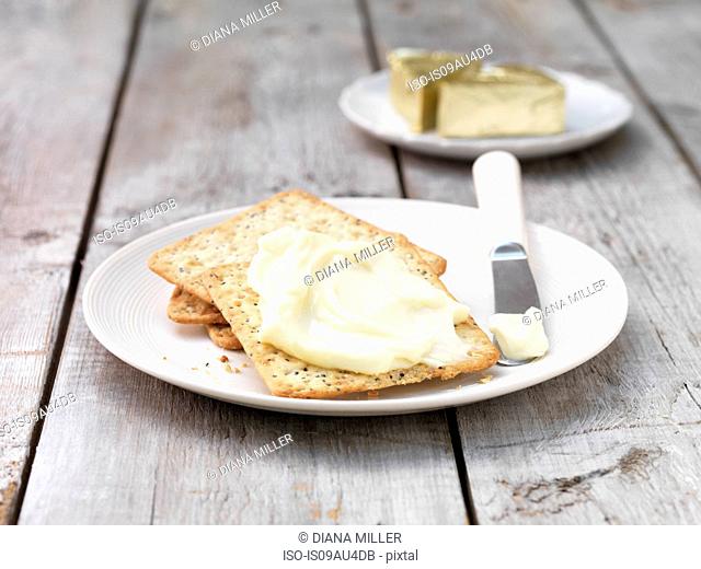 Soft cheese triangles smeared on square crackers with butter knife on plate