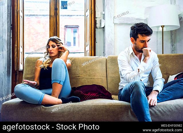 Couple sitting on sofa apart and being angry after quarrel
