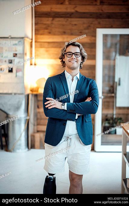 Happy young businessman with arms crossed standing in office